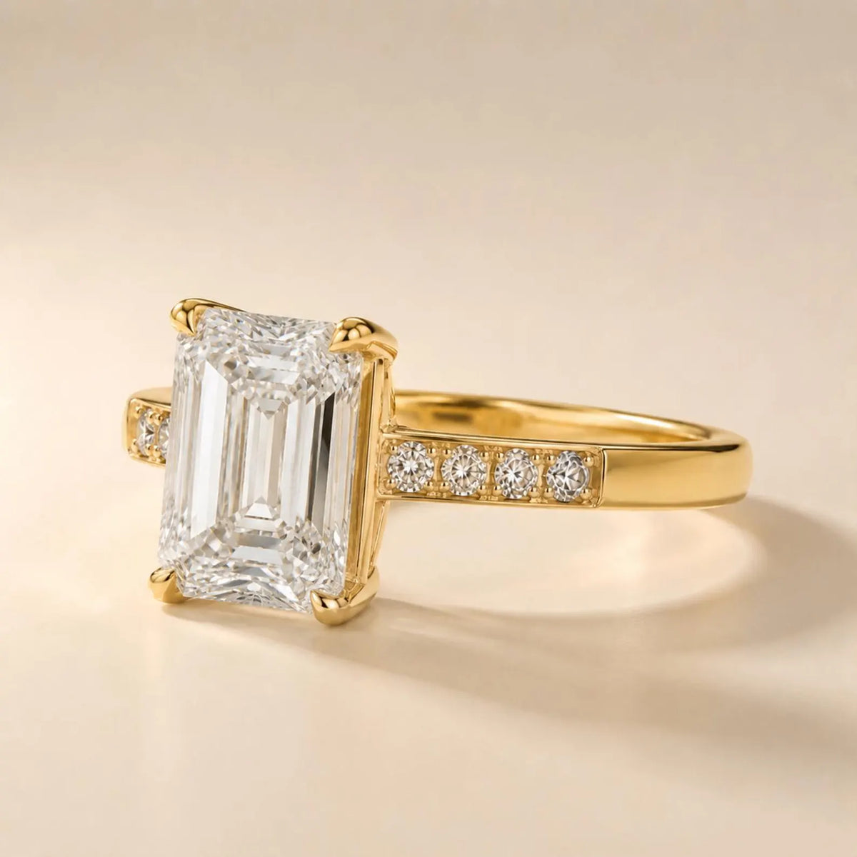 Angled side profile showing step-cut clarity of a 4 CT emerald cut lab diamond and channel-set accent stones in yellow gold.