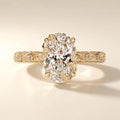 Top view of a 4 CT oval lab grown diamond ring featuring leaf motif claw prongs and an engraved botanical vine band in yellow gold.