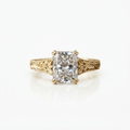 Front view of a 4 CT radiant cut lab diamond ring set with double claw prongs on an engraved leaf-motif yellow gold band.