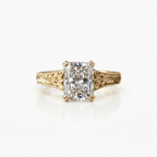 Front view of a 4 CT radiant cut lab diamond ring set with double claw prongs on an engraved leaf-motif yellow gold band.