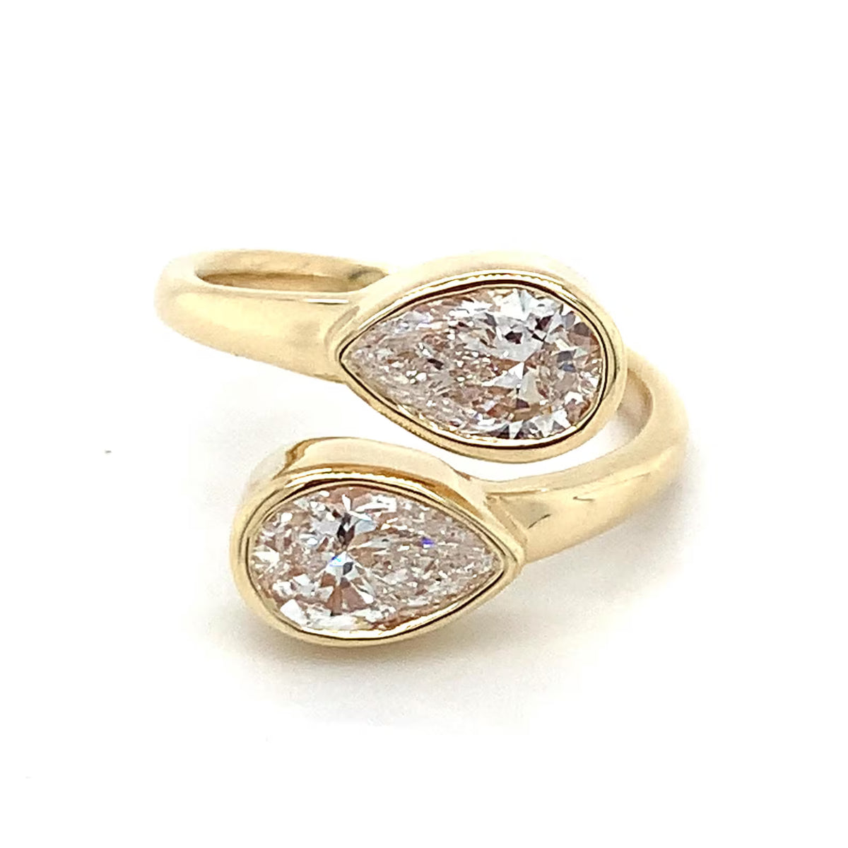 Angled side view of an open cuff bypass ring showcasing two pear cut lab diamonds in solid yellow gold bezel frames.