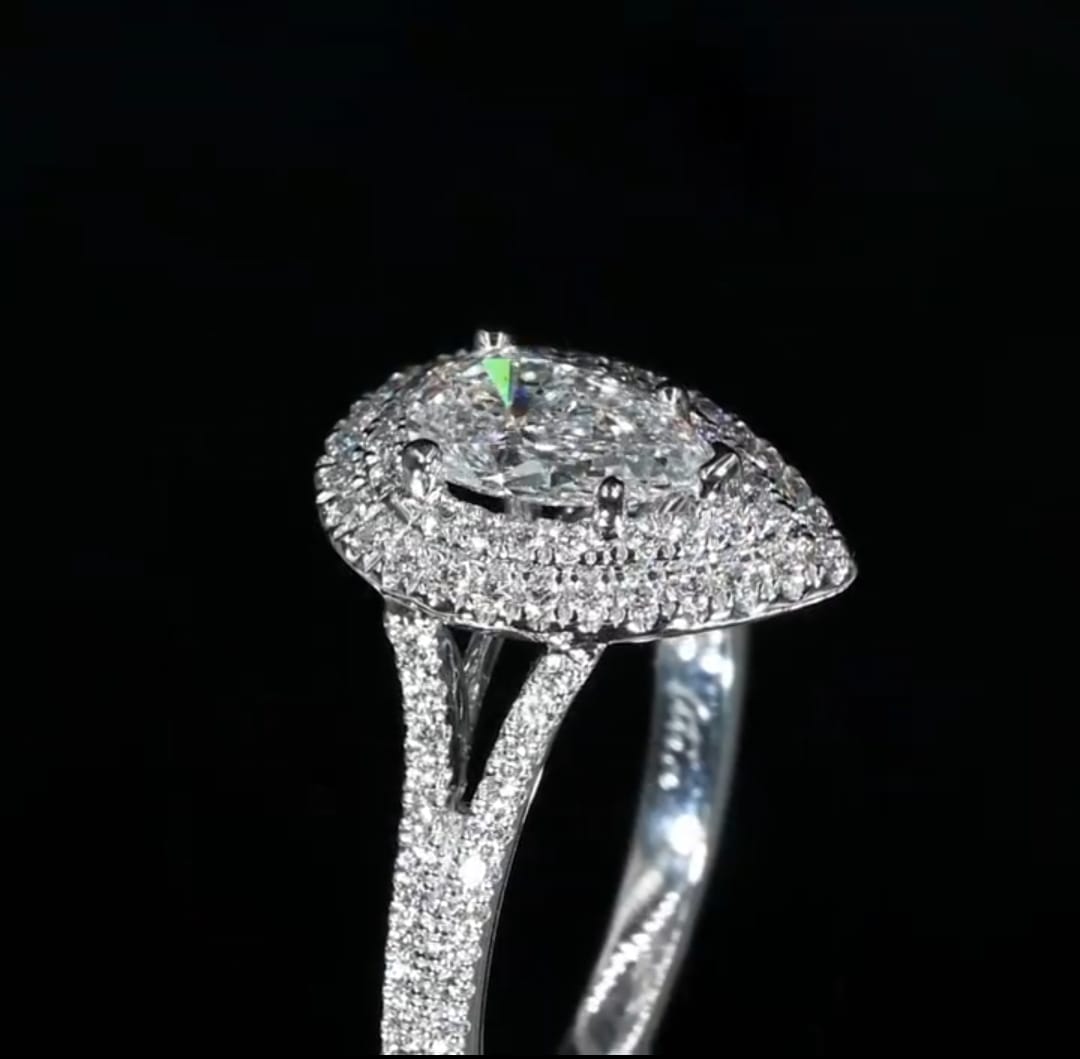 High angle side profile of a 3 CT pear cut lab grown diamond ring showcasing a raised double halo and a diamond-encrusted split shank band against a dark background.