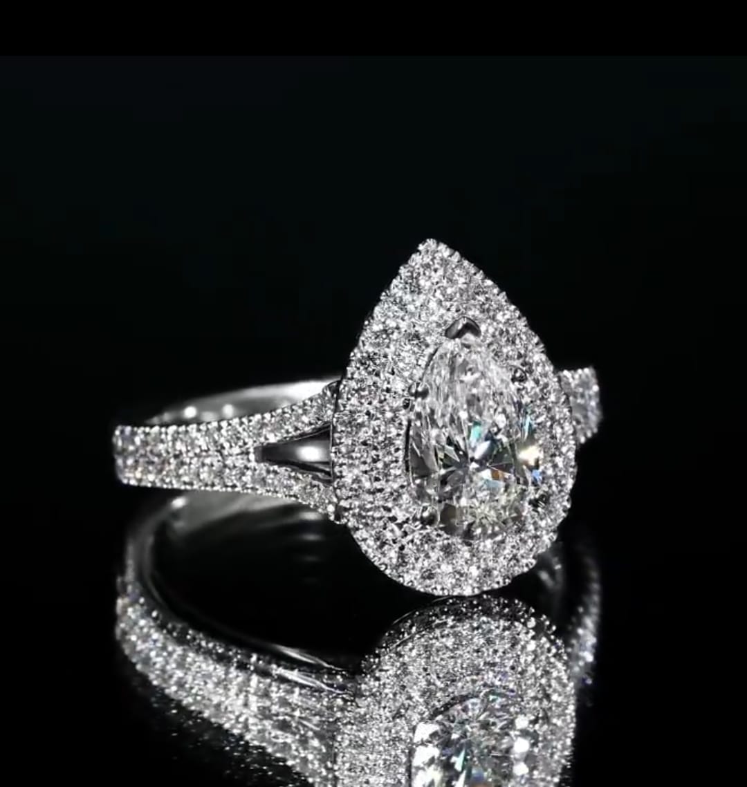 Angled top view of a 3 carat pear shaped lab diamond ring showing the spectacular double halo resting on a black reflective surface.