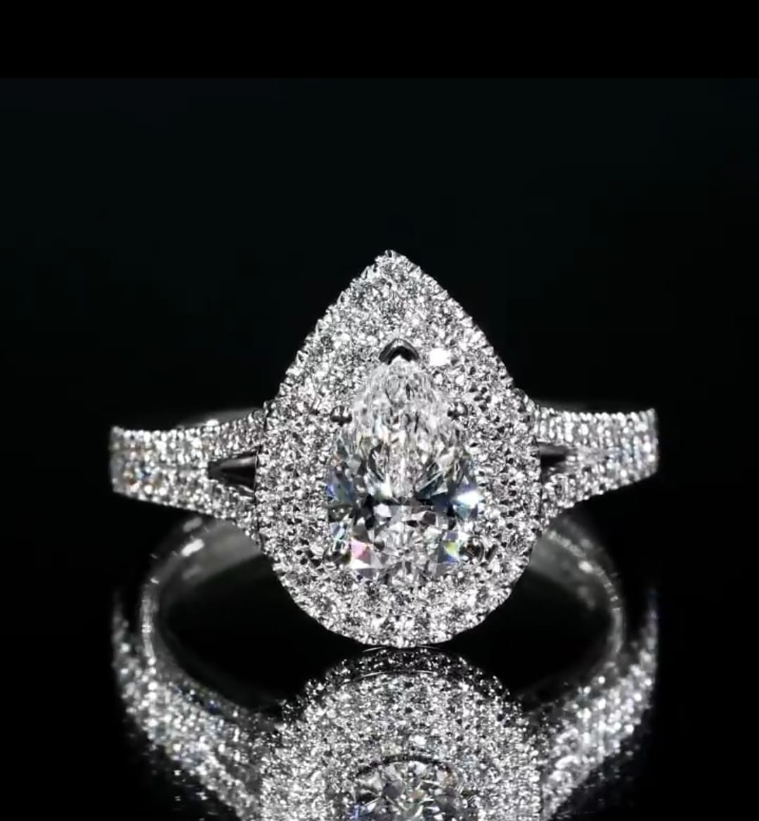 Direct top-down view of a pear cut double halo diamond engagement ring reflecting brilliantly on a dark mirror background.