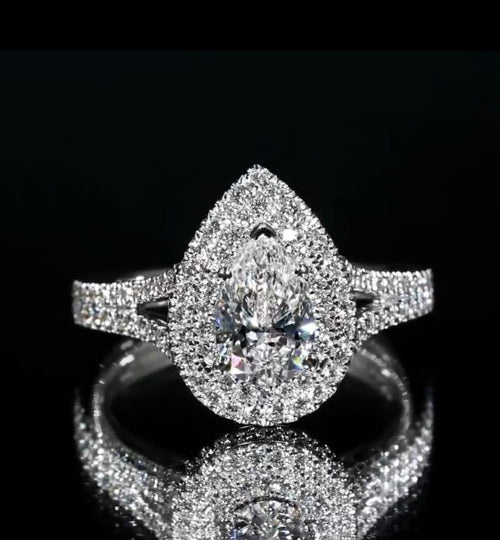 Direct top-down view of a pear cut double halo diamond engagement ring reflecting brilliantly on a dark mirror background.