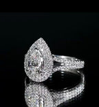 Three-quarter angled shot of a dazzling pear cut split shank engagement ring glowing with intense diamond fire on a black surface.