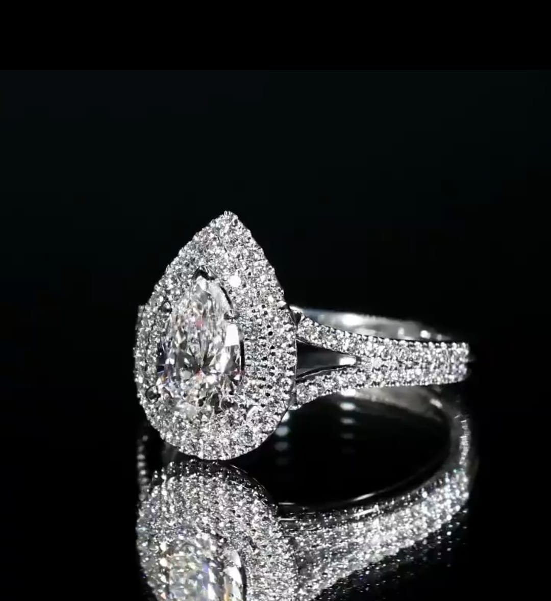 Three-quarter angled shot of a dazzling pear cut split shank engagement ring glowing with intense diamond fire on a black surface.