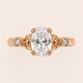 Top view of a 3 CT oval cut lab grown diamond engagement ring with leaf motif shoulders and bezel side diamonds in rose gold.