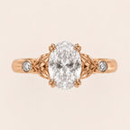 Top view of a 3 CT oval cut lab grown diamond engagement ring with leaf motif shoulders and bezel side diamonds in rose gold.