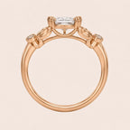 Side profile view of a rose gold 3 carat oval lab diamond ring showing double claw prongs and carved leaf setting.