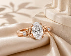 Aesthetic display of a 3 carat oval lab diamond leaf motif engagement ring resting on beige silk.