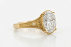 Side profile view showing claw prongs, milgrain border, and hand-engraved leaf motif on a 5 CT oval lab diamond ring.