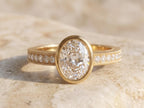 Top view of a 3 carat oval cut lab diamond set in a sleek yellow gold bezel with a vintage milgrain channel-set band.