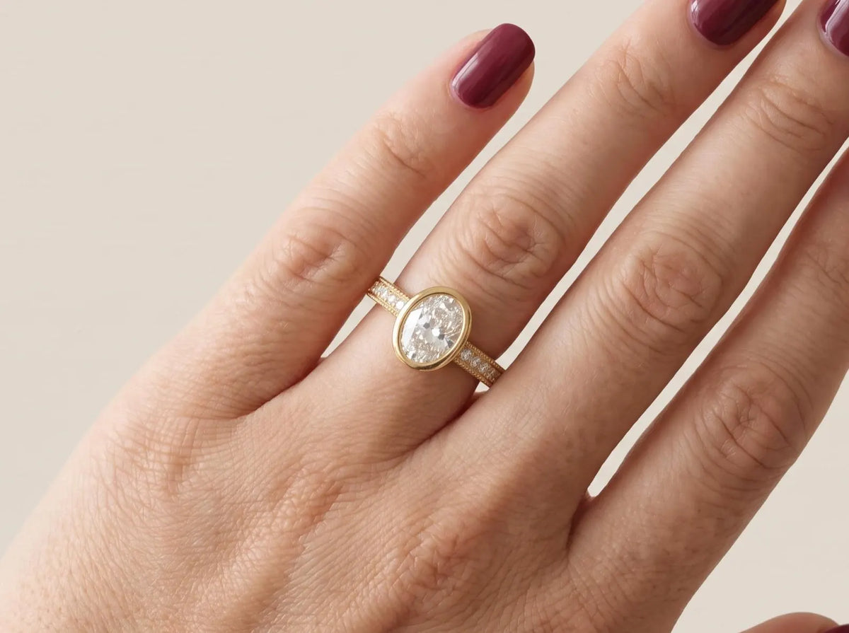 On-hand view of a 3 CT oval cut lab grown diamond bezel engagement ring in yellow gold.