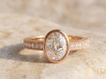 Front view of a 3 CT oval cut lab grown diamond bezel set engagement ring in warm rose gold.