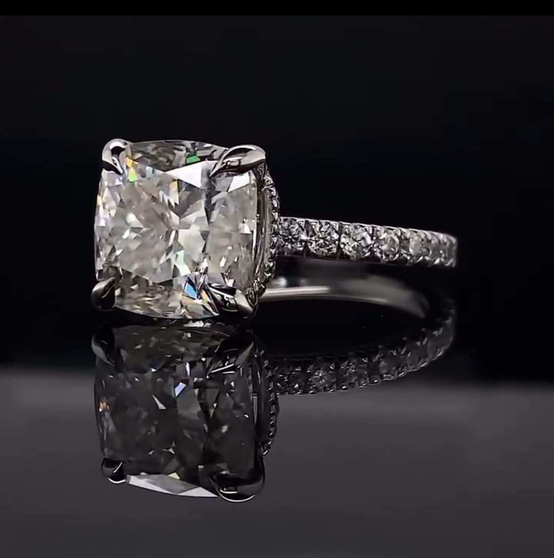 High angle view showing the soft rounded corners, elegant claw prongs, and pave band of a stunning cushion cut diamond ring.