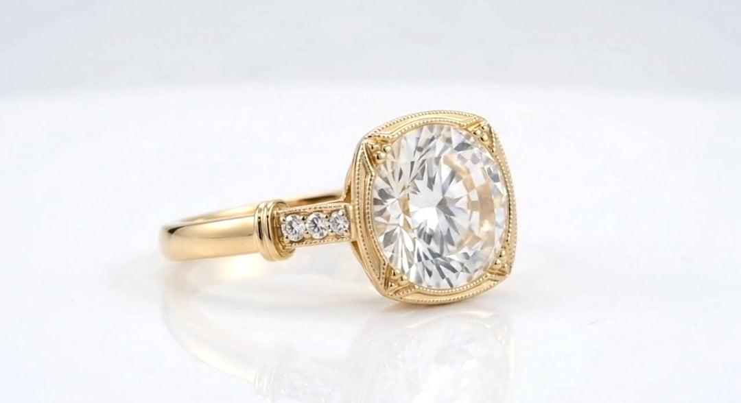 Angled side view of a 4 carat round cut lab diamond framed in a cushion-shaped milgrain border with shoulder diamond accents.