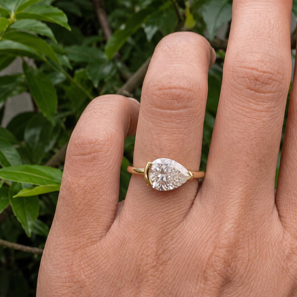 On-hand view of a 2 CT East-West horizontally set pear cut lab grown diamond ring in yellow gold with half-bezel setting.