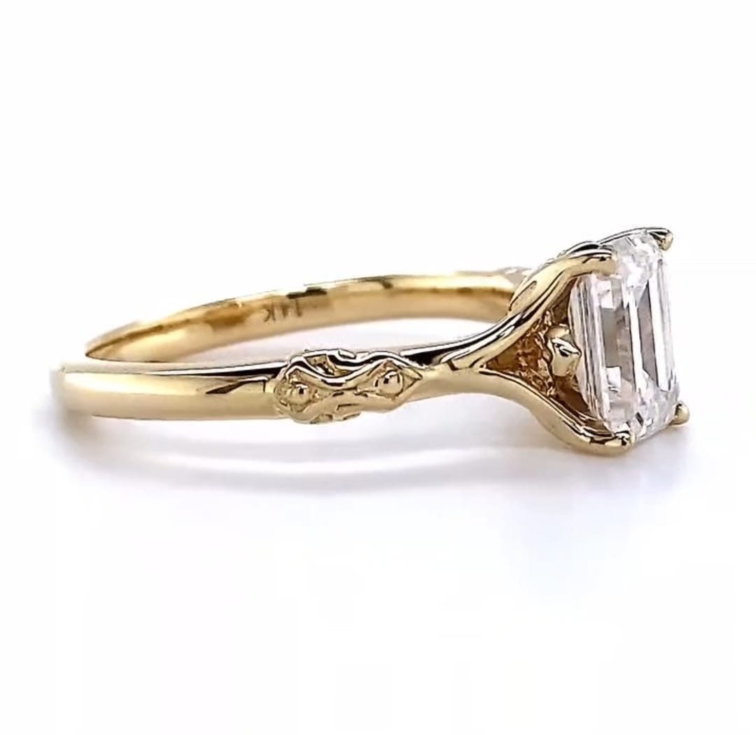 Side profile view of a yellow gold 3 CT emerald cut lab grown diamond engagement ring highlighting the sculpted vintage scrollwork on the band.