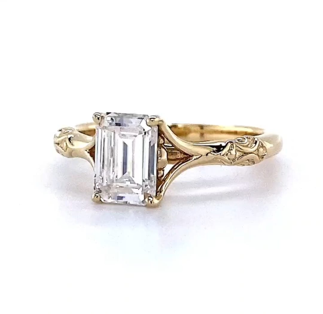 Front three-quarter angle view of a 3 CT emerald cut diamond ring displaying step-cut clarity and embossed relief detailing on the shank.
