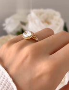 Side-angle perspective on finger displaying the setting height, pave halo border, and textured gold band.