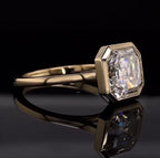 Perspective view on a reflective surface displaying the yellow gold bezel setting around the 4 CT Asscher diamond