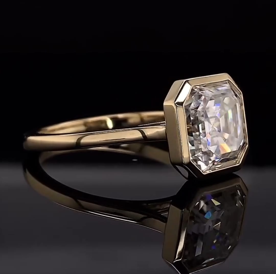 Perspective view on a reflective surface displaying the yellow gold bezel setting around the 4 CT Asscher diamond