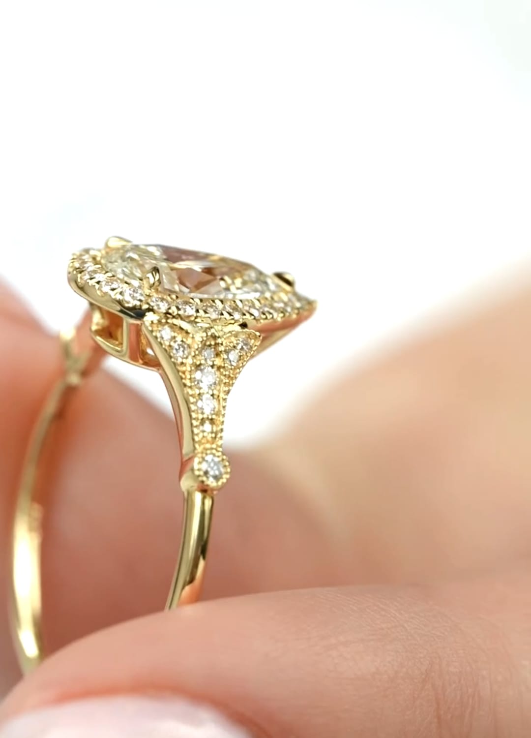 Close-up side profile showing the intricate milgrain and pavé shoulders of a yellow gold pear diamond ring