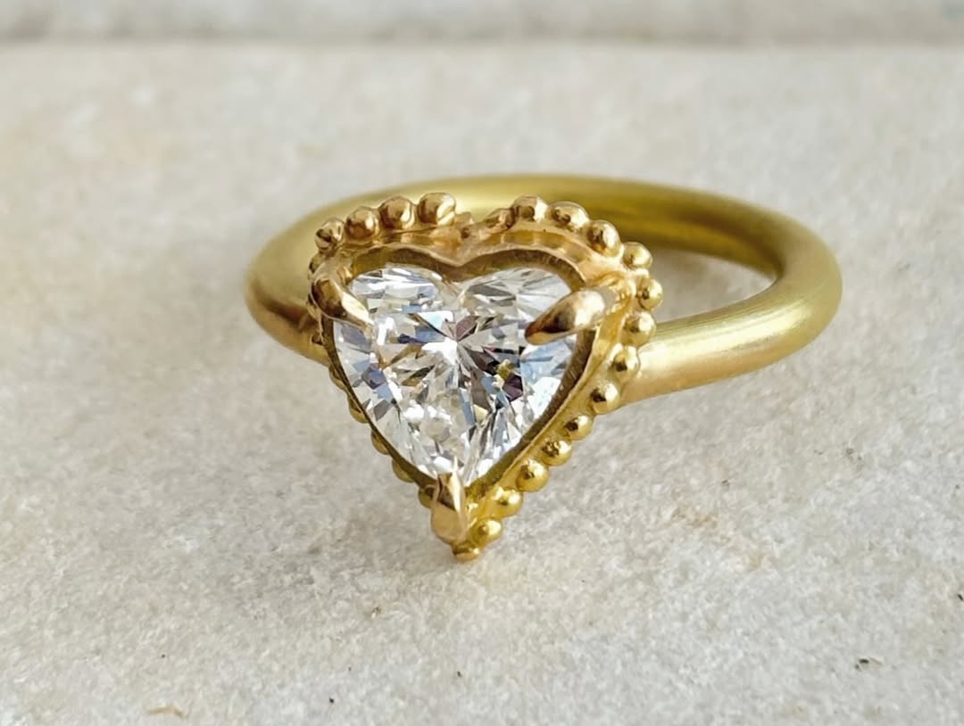 Three-quarter view of a 2 CT heart cut lab grown diamond ring with a beaded gold frame and satin yellow gold band