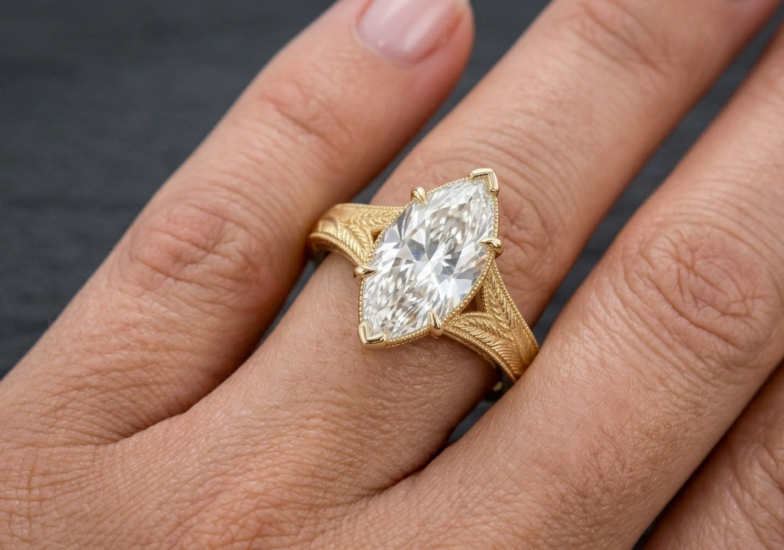 On-hand view showcasing a 3 CT marquise cut lab grown diamond engagement ring with hand-engraved leaf band in yellow gold