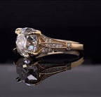 Angled view highlighting the petaled split shoulder filigree and double prong setting on a reflective dark surface