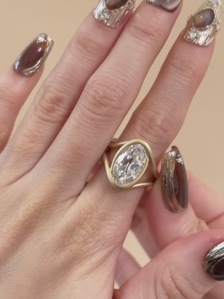 3 CT oval lab grown diamond engagement ring with a fluid, matte gold swirl bezel setting.